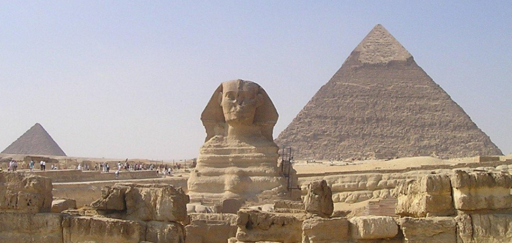 Great Pyramid and Sphinx at Giza with visitors and stone walls under a clear blue sky.