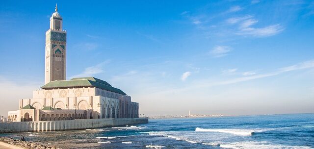 Casablanca's Hassan II Mosque beside the Atlantic, with a tall minaret and arched exterior along a seawall.