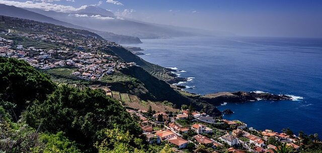 Coastal village perched on a steep hillside overlooking the blue ocean with terraced fields and rocky cliffs along the coast.